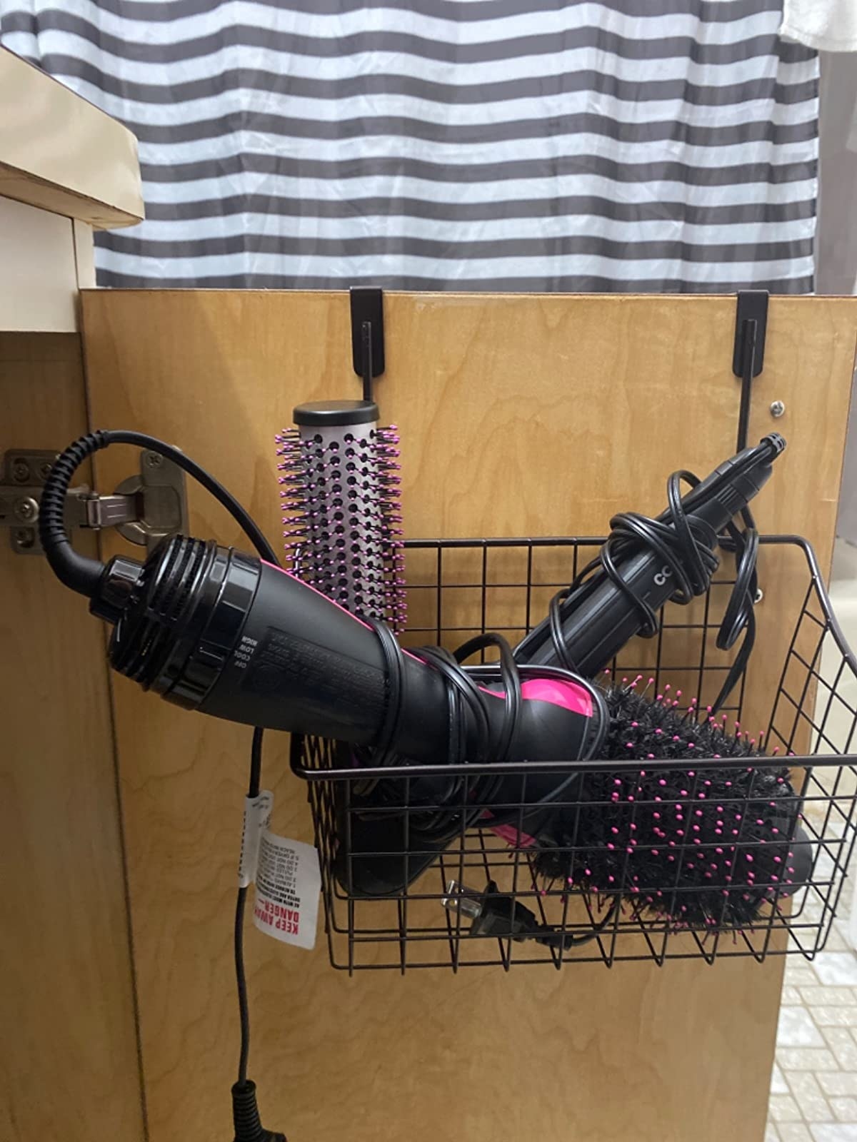 Reviewer image of basket hanging on a cabinet door holding hair styling tools