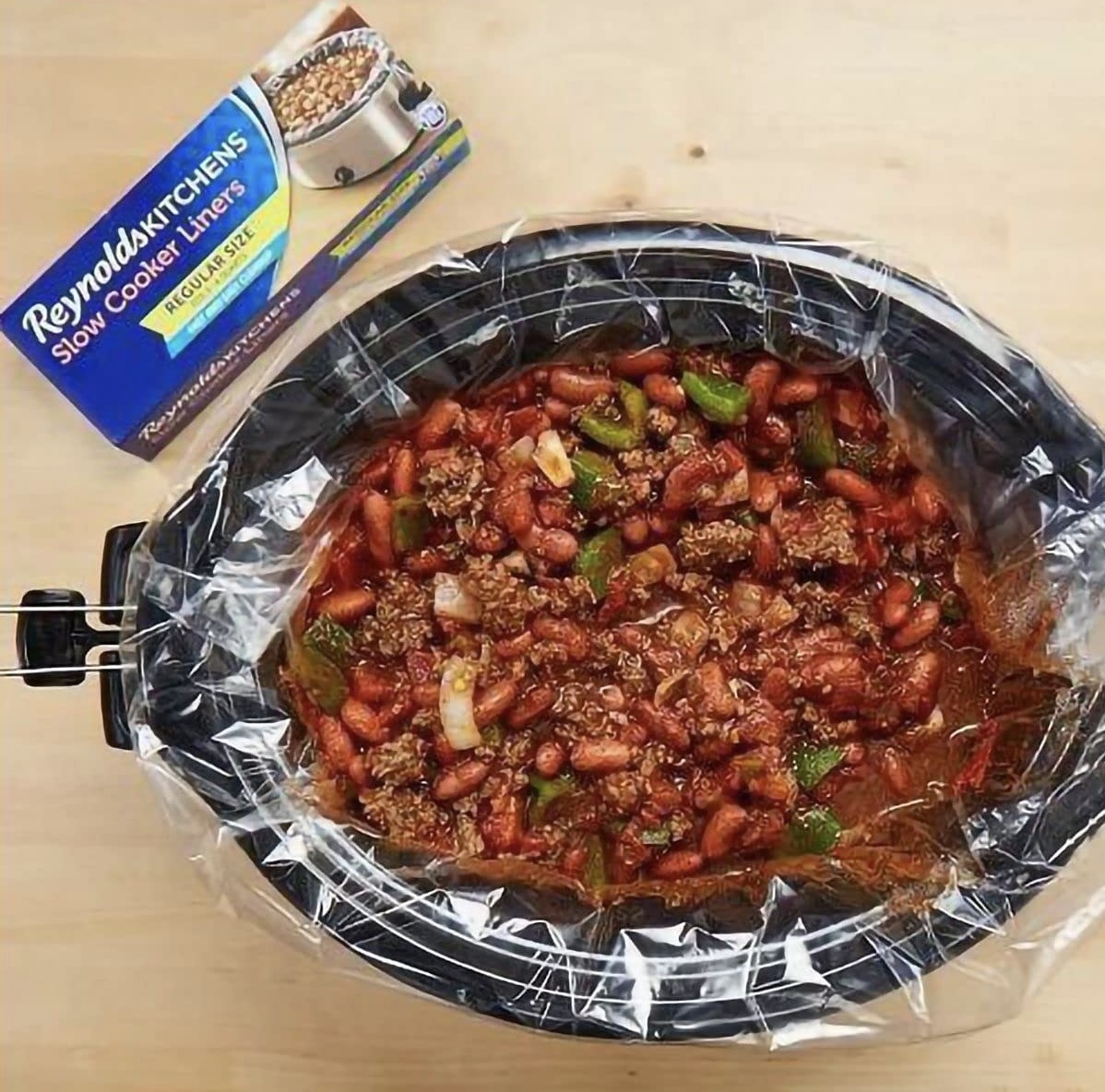 A crockpot with a liner in it with chili inside of it