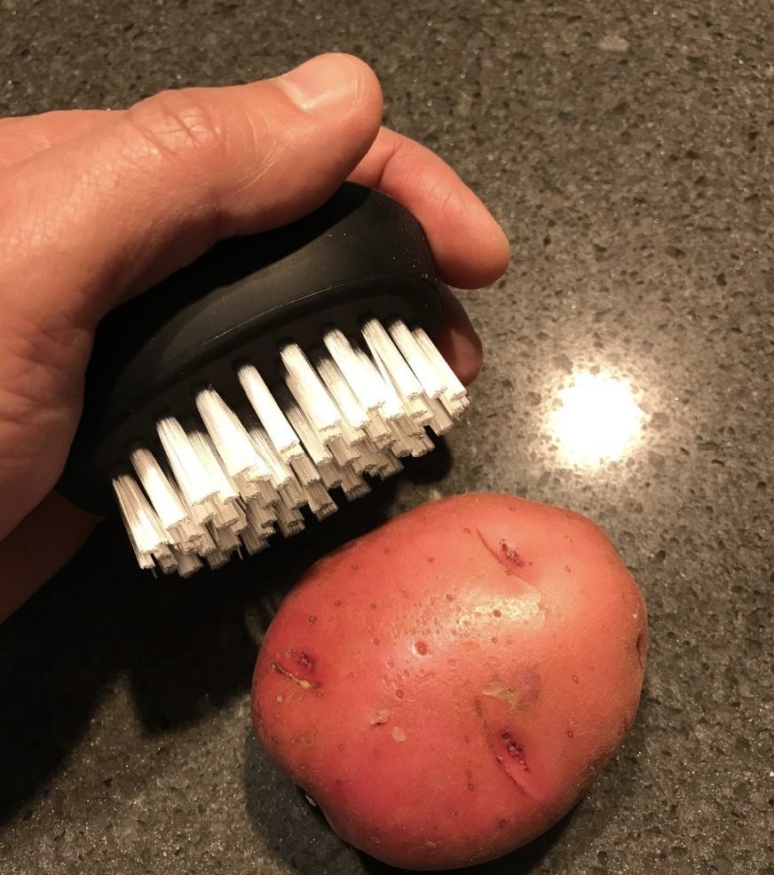 someone holding the brush in black next to a red potato