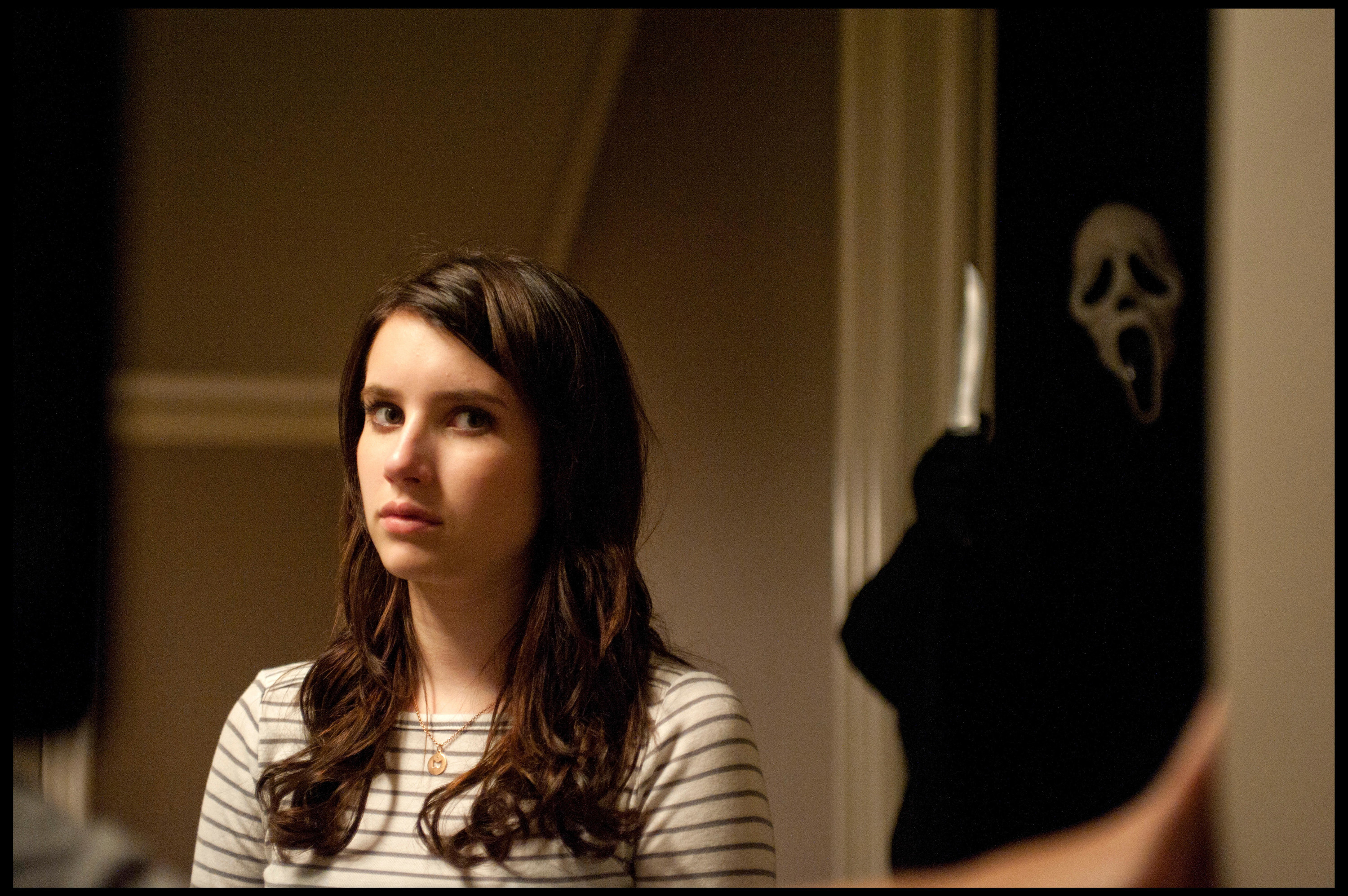 Emma Roberts stares at an off-screen figure while a Ghostface killer sneaks behind her