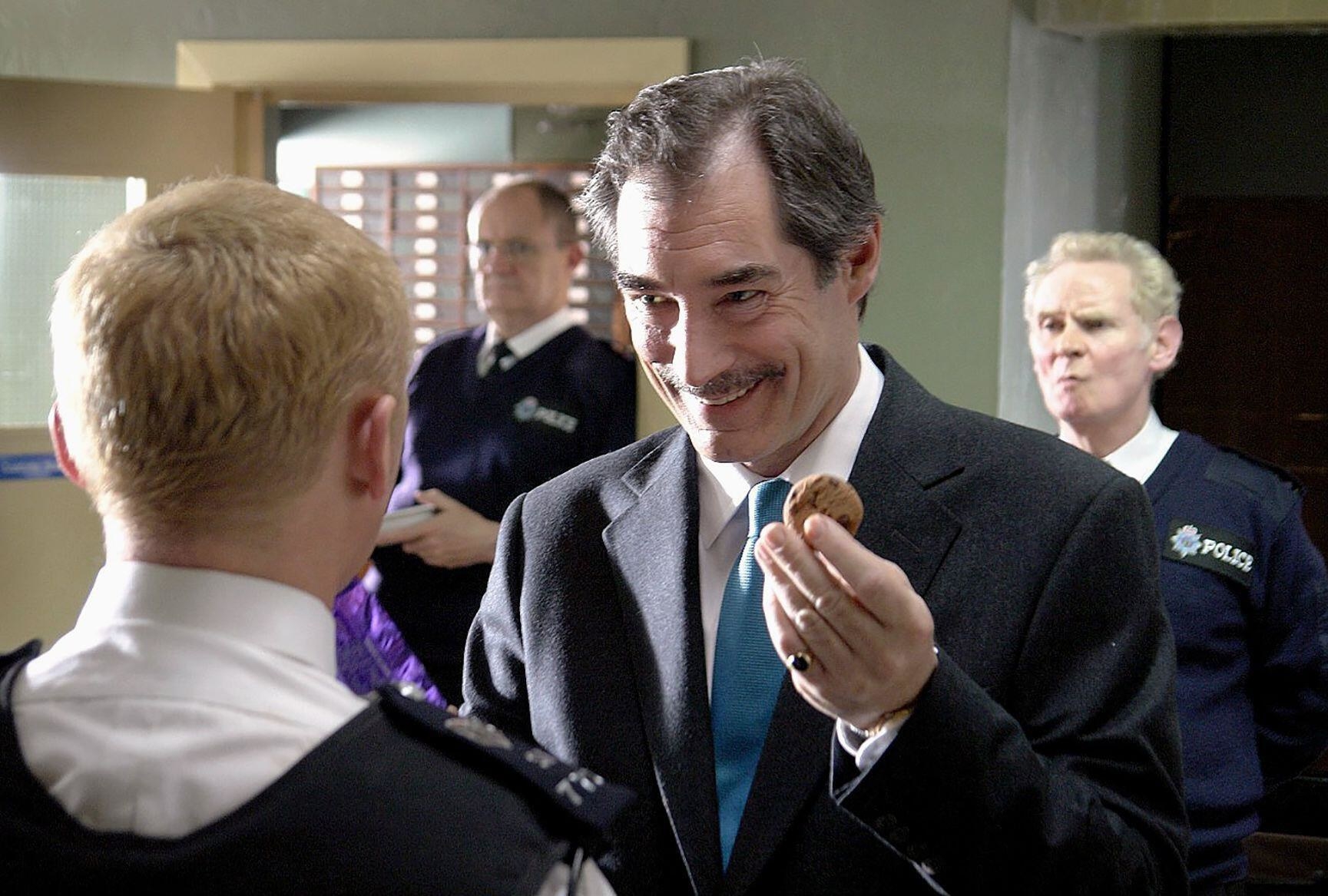 A devious man smiles and offers a police officer a cookie