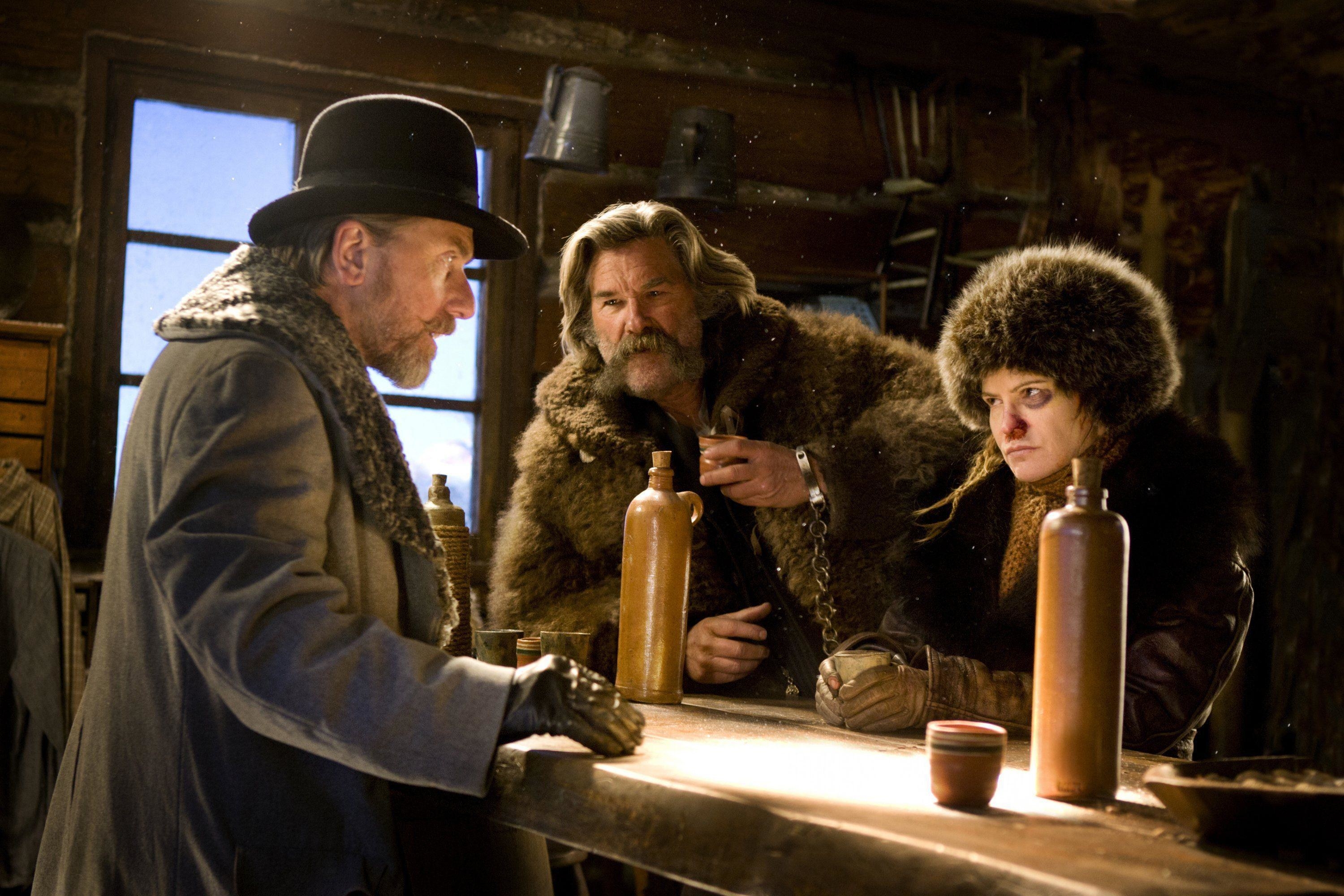 Tim Roth, Kurt Russell and Jennifer Jason Leigh, adorned in heavy, fur clothing, assemble around a wooden table