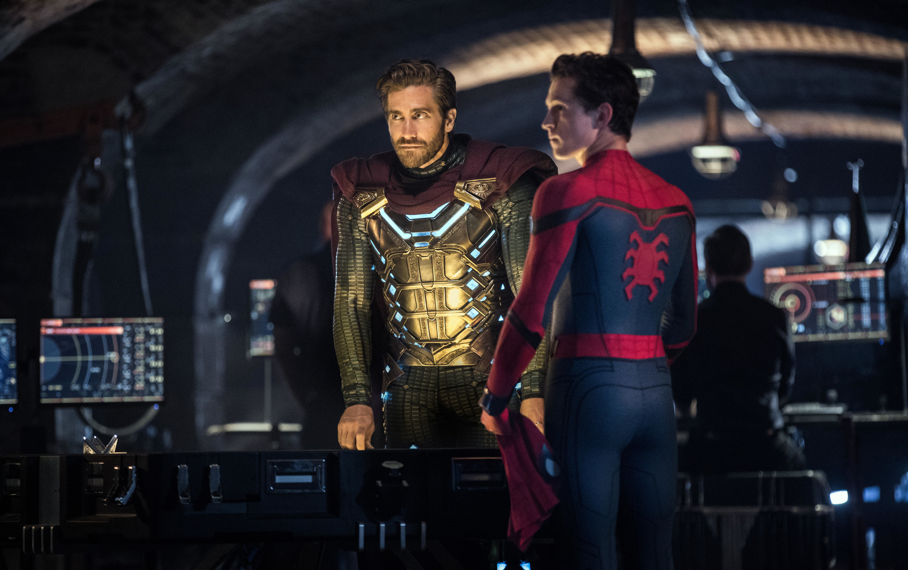 Jake Gyllenhaal and Tom Holland, wearing their respective super-suits, stand around a futuristic laboratory