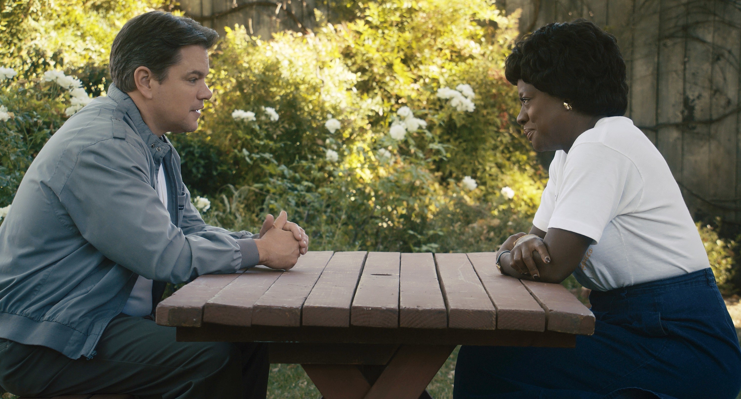 A man and a woman sit across from each other at a picnic table, talking