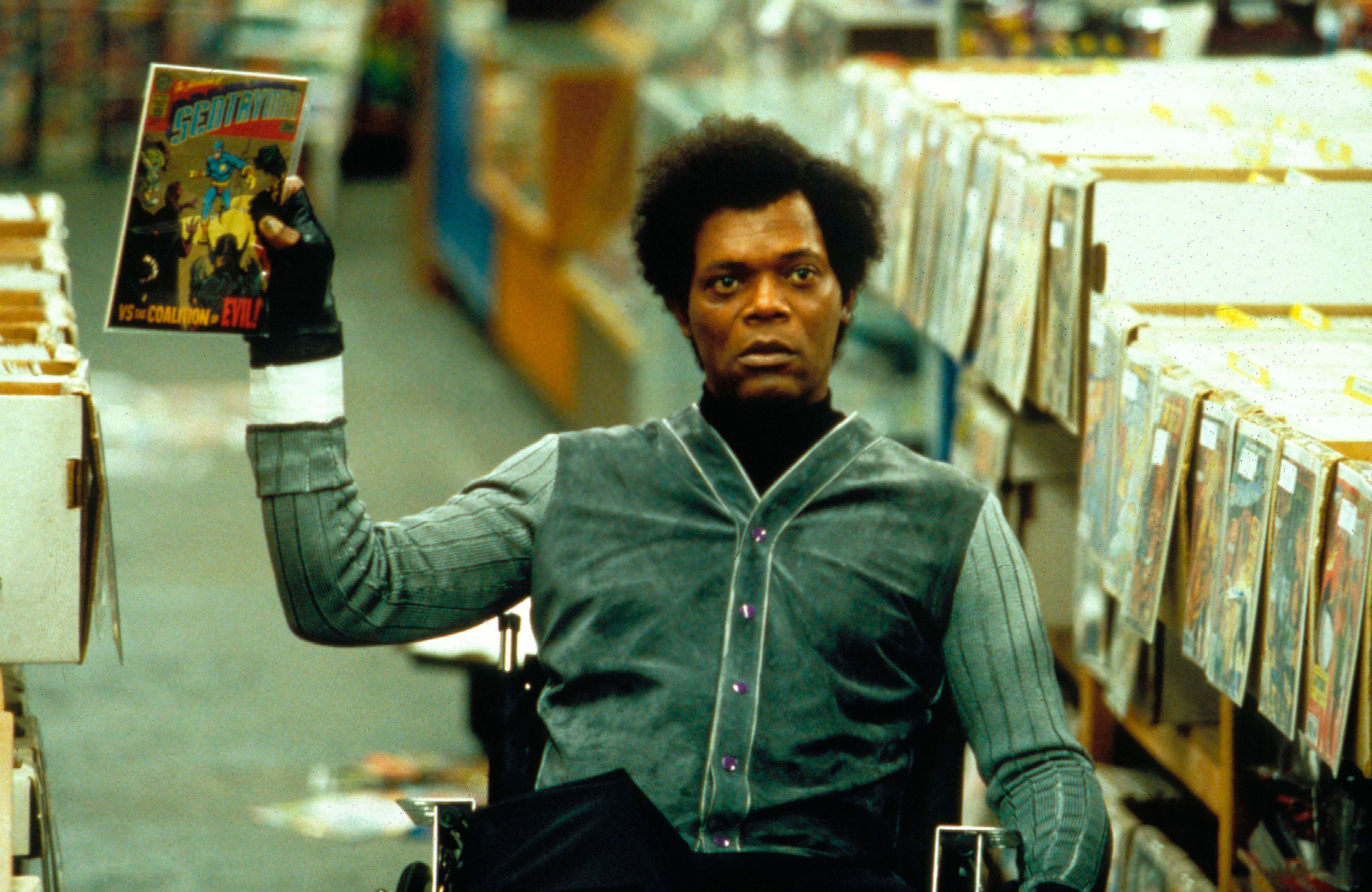 Samuel L. Jackson in a wheelchair holds up a comic book