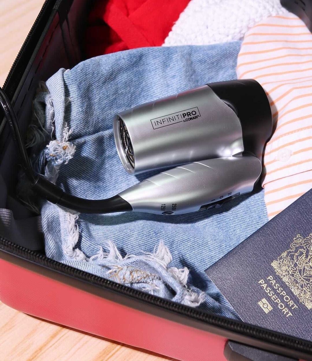 the folded hair dryer tucked into a suitcase with clothing and a passport