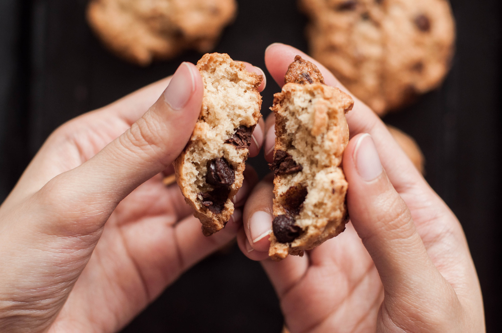 A person holding a chocolate chip cookie torn into halves