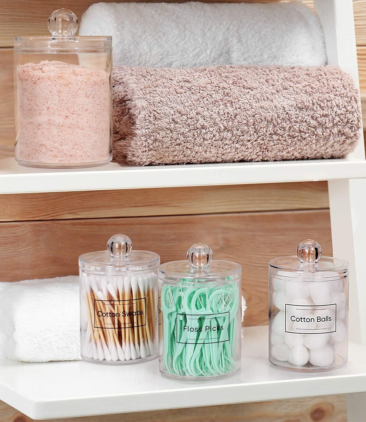 the jars filled with things on a ladder shelf in a bathroom