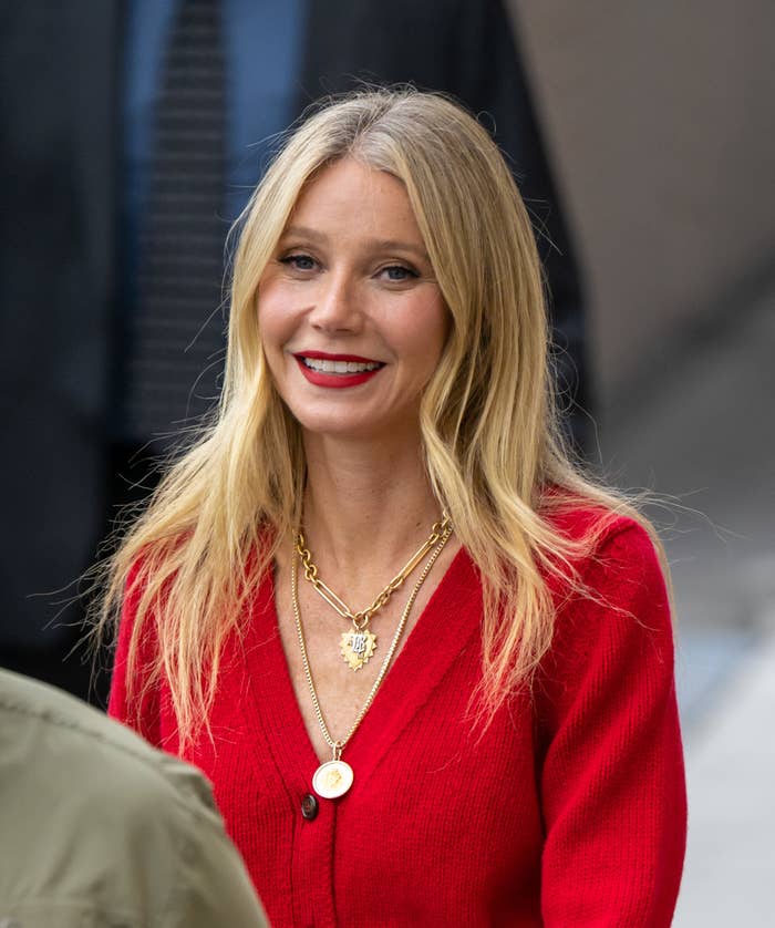 Gwyneth outside wearing a cardigan, several necklaces, and bold red lipstick