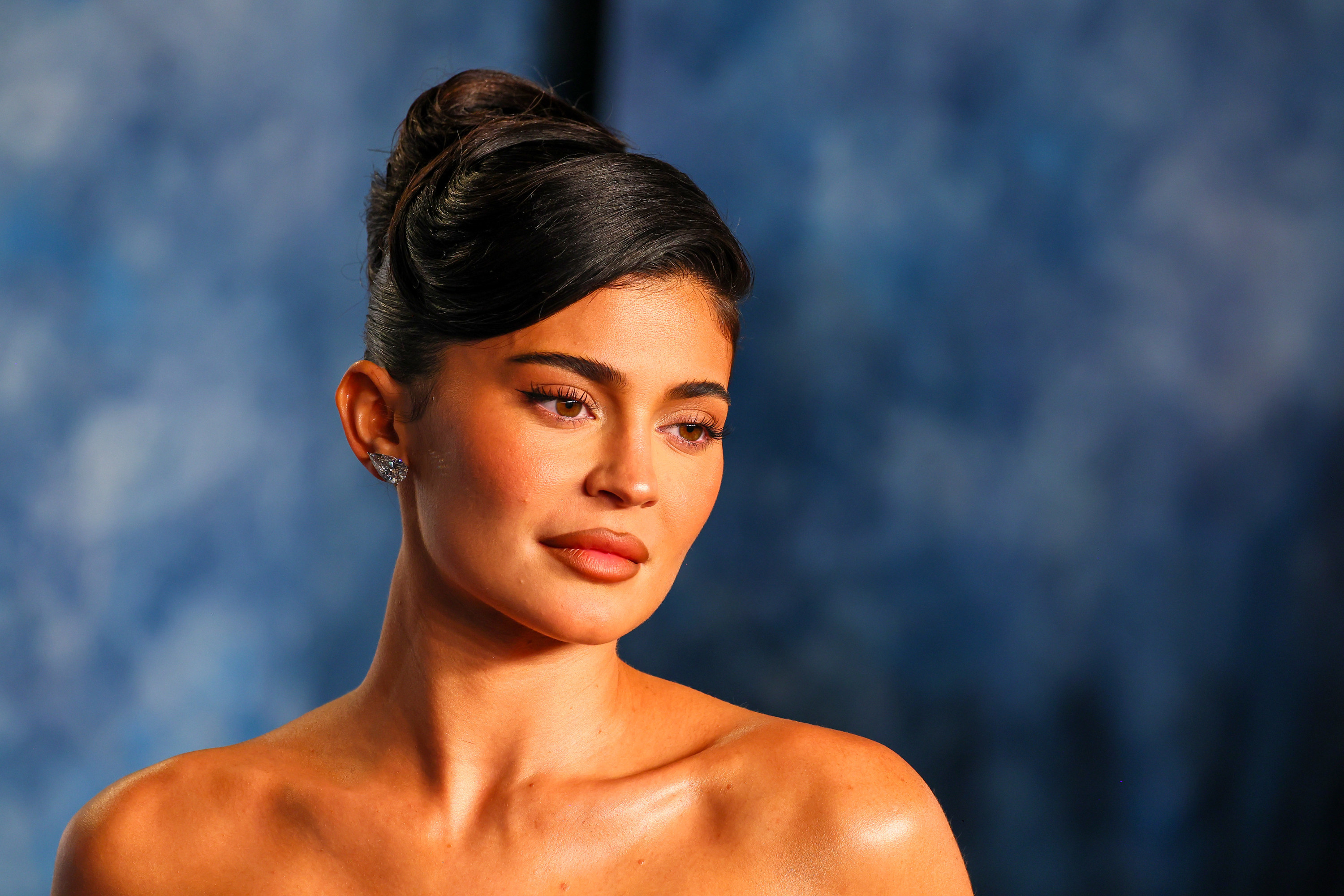A head and shoulders shot of Kylie, her face neutral, wearing a strapless dress with her hair piled up on top of her head