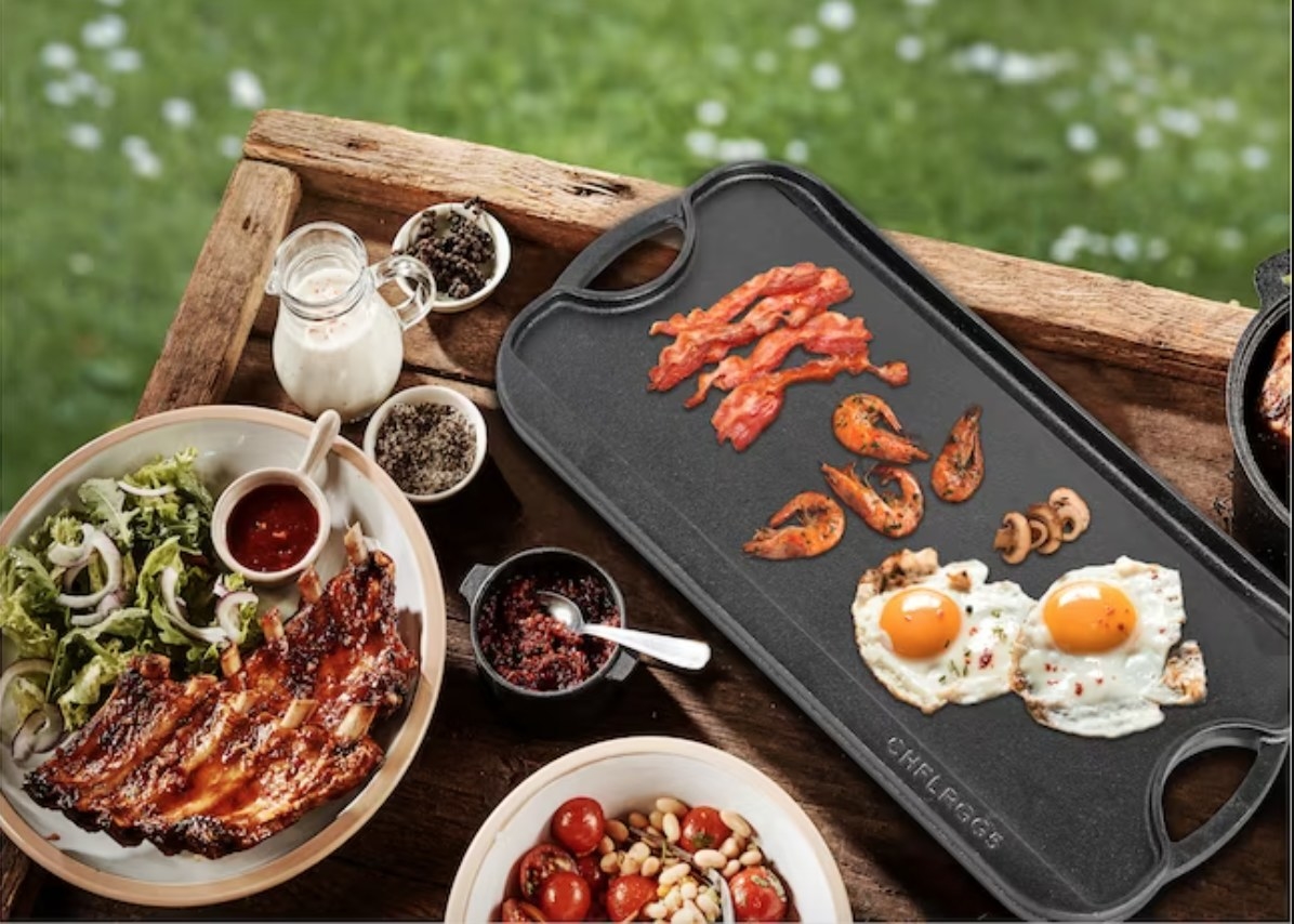 a cast iron griddle cooking eggs, shrimp, and bacon surrounded by other food and seasonings on top of a wooden tray