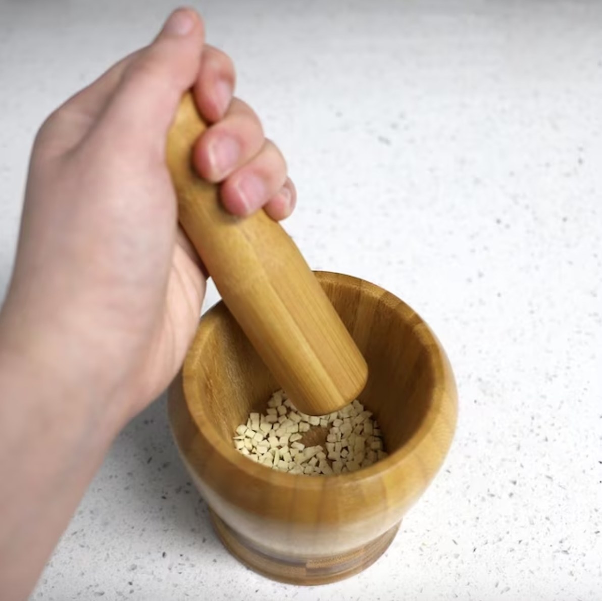 A person grinding herbs with a bamboo mortal and pestle