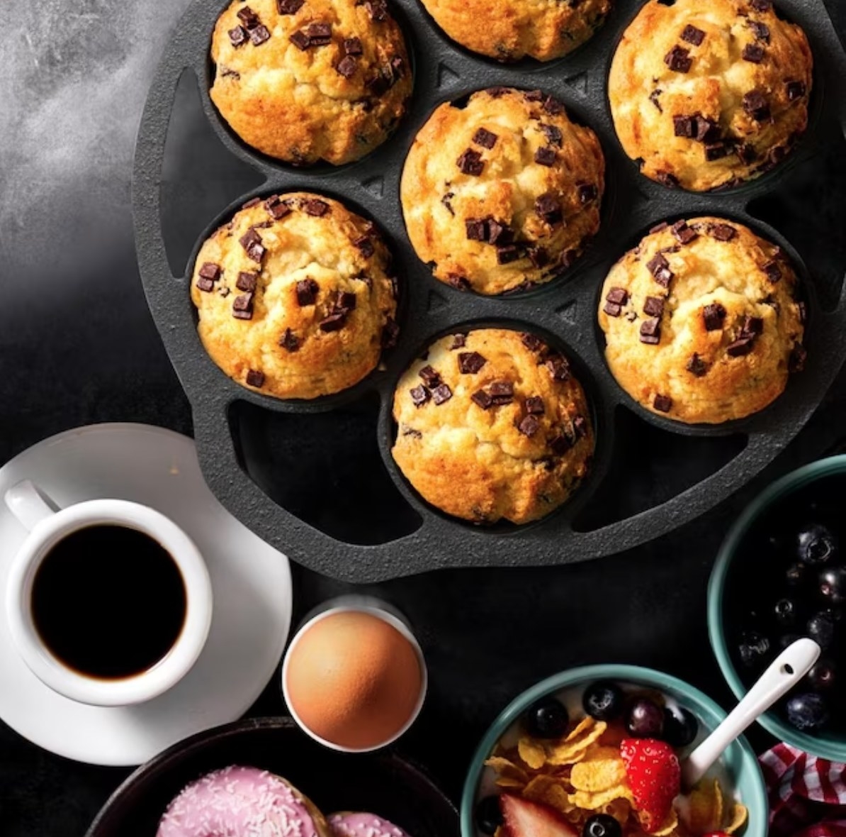 a cast iron biscuit pant with baked muffins in it surrounded by breakfast foods