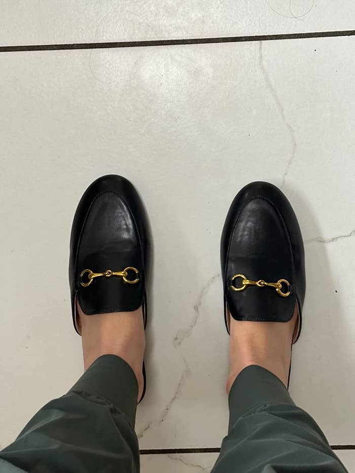 reviewer wearing the mules in black with gold buckle