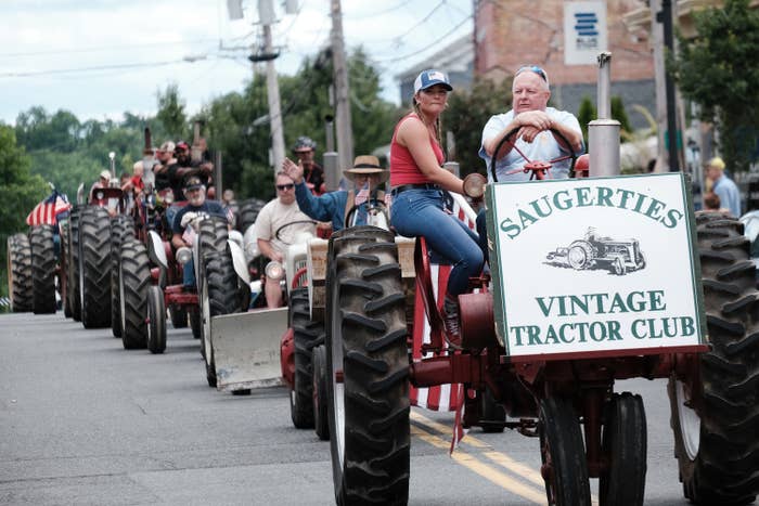 Tractors in the middle of the street with a sign that says "Saugerties Vintage Tractor Club"