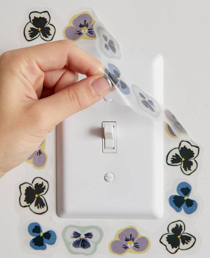a person putting a floral decal around a light switch