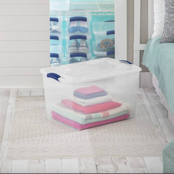a photo of a clear bin on a bedroom floor with a stack of towels inside