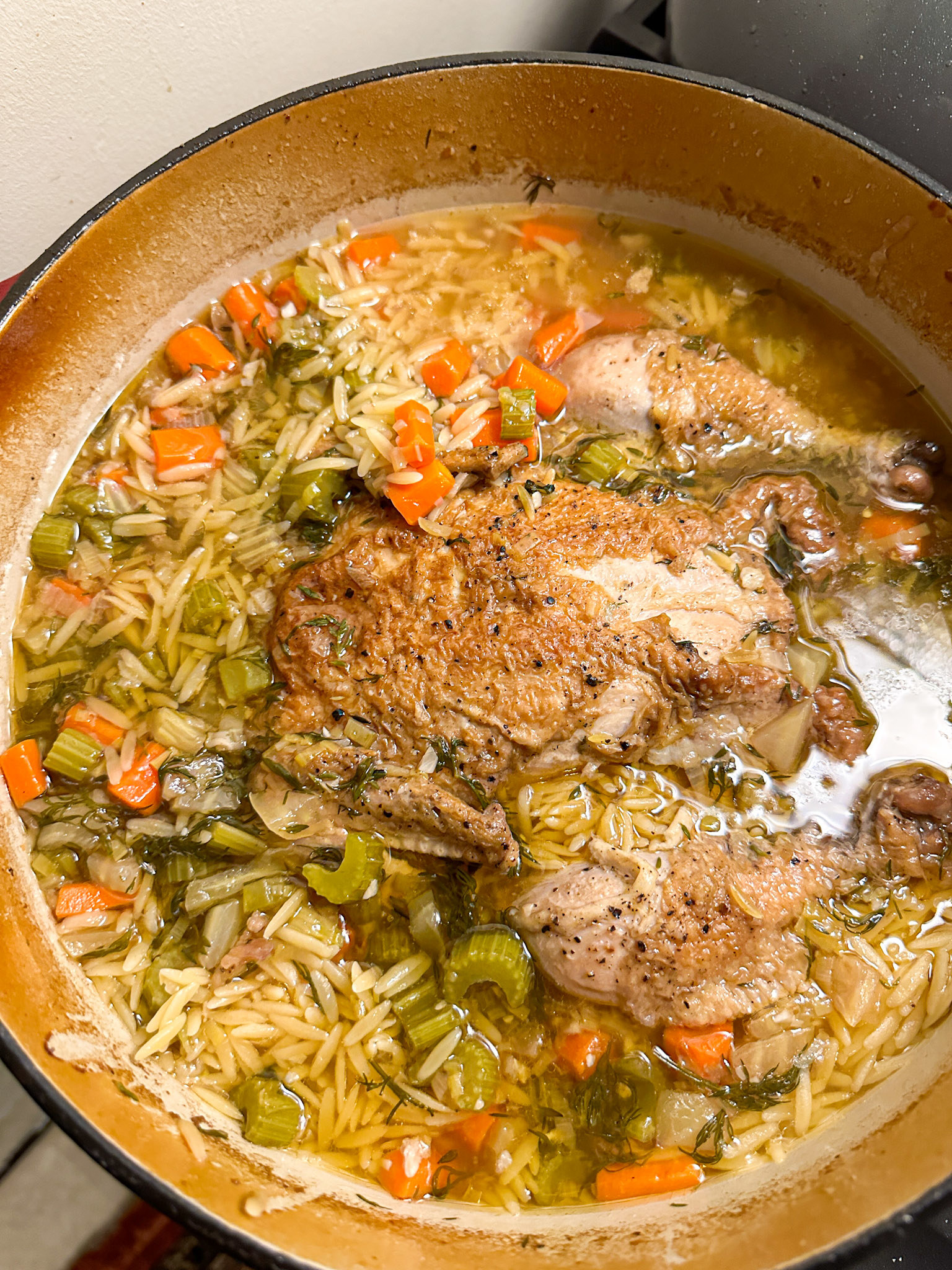 Dutch oven with a whole chicken inside, along with orzo and veggies in broth