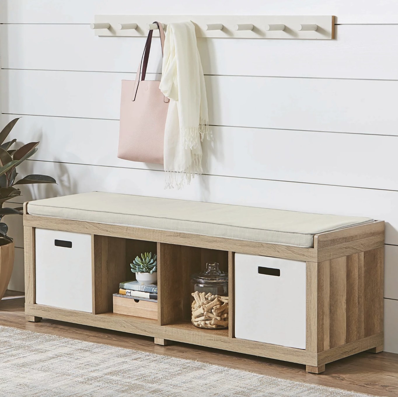the light wood bench with two bins and decorations in a styled entryway space