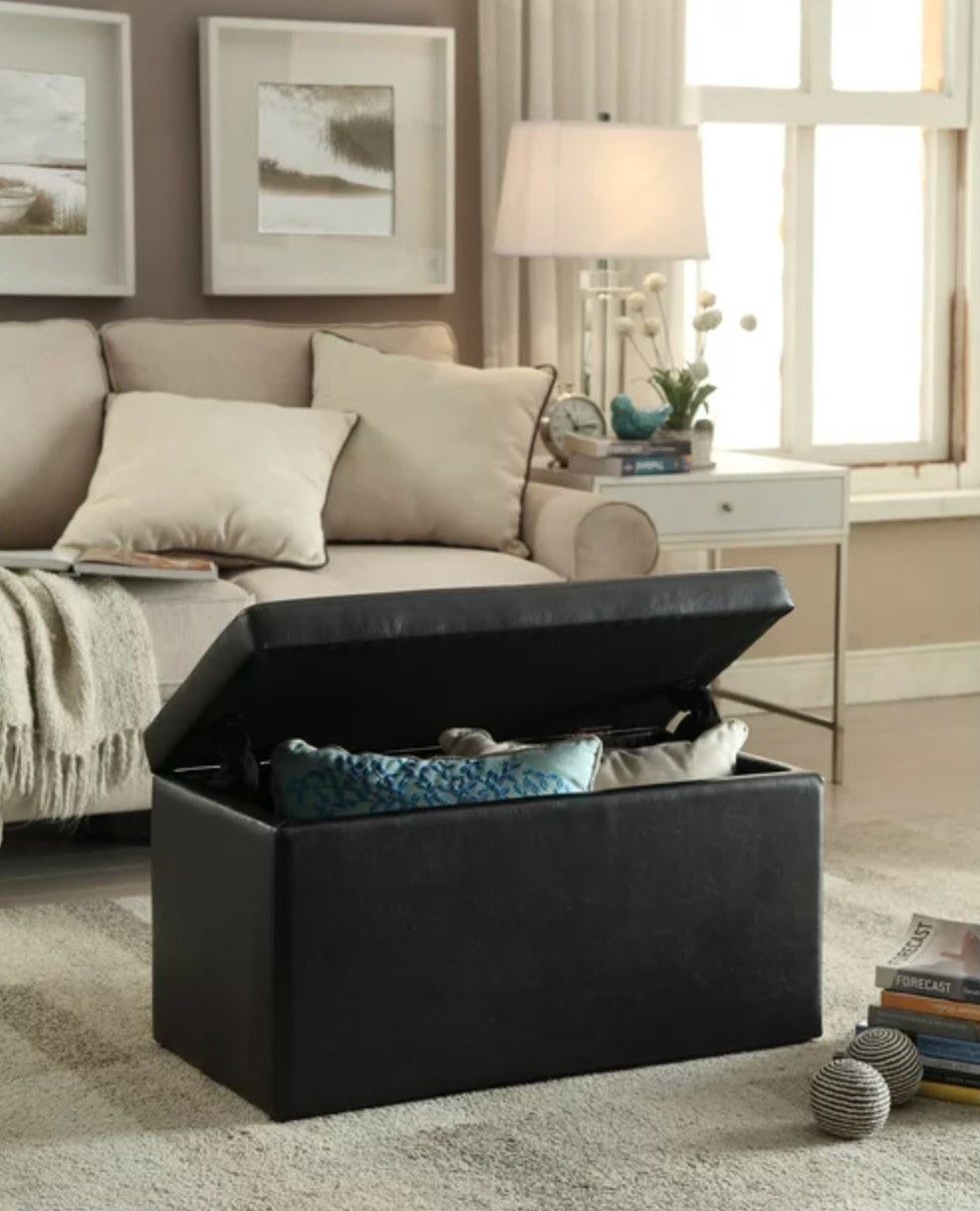 the black faux-leather ottoman in the middle of a living rom with pillows inside