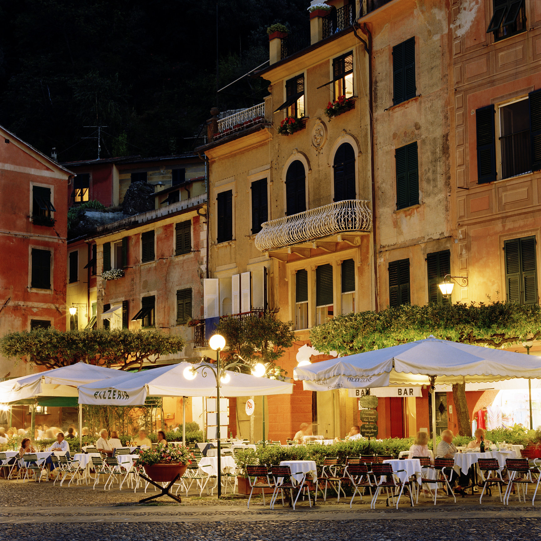 People dining outside in a piazza at night.