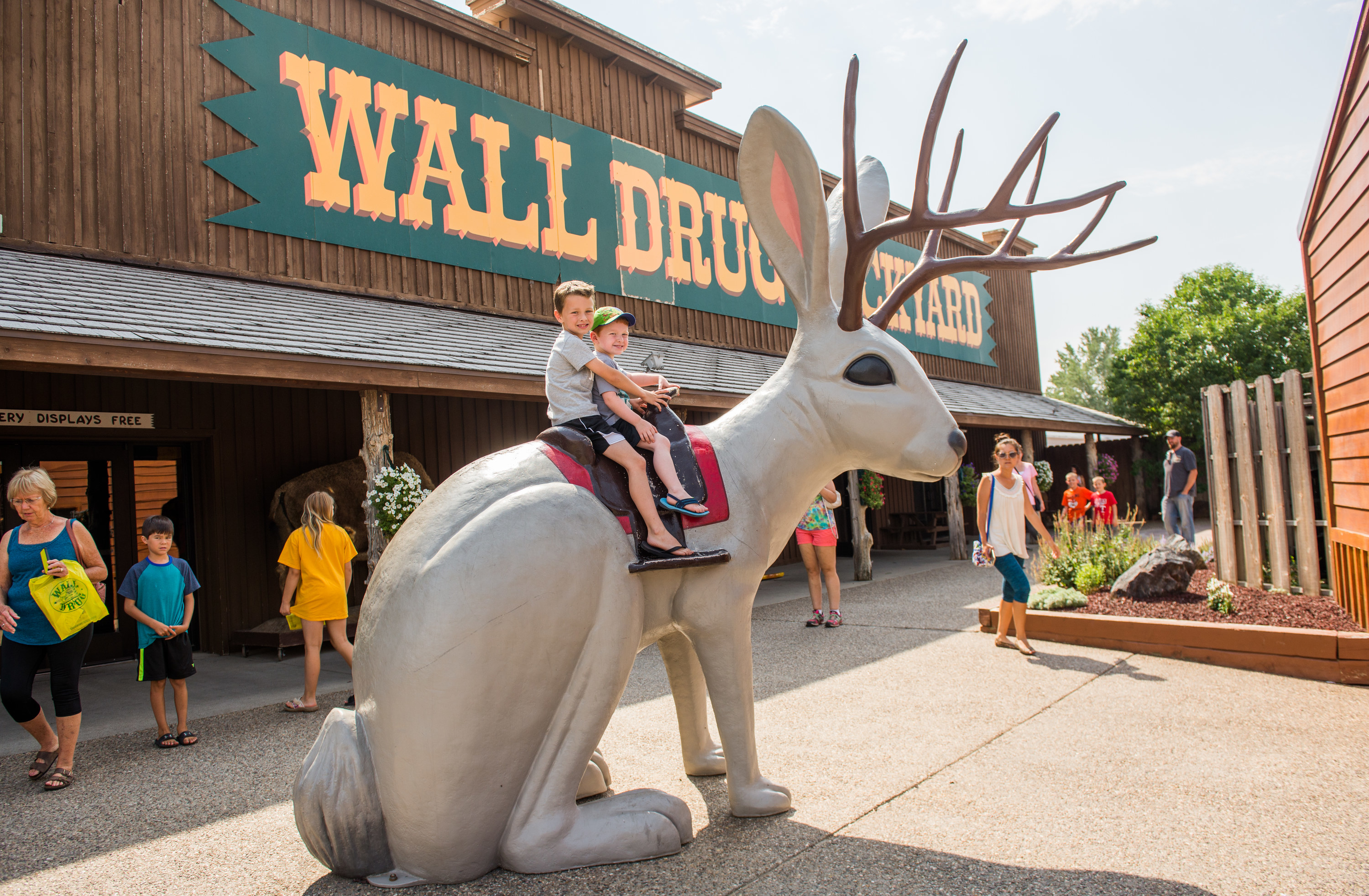 Kids on a statue of a jackalope in front of storefront that says &quot;Wall Drug&quot;