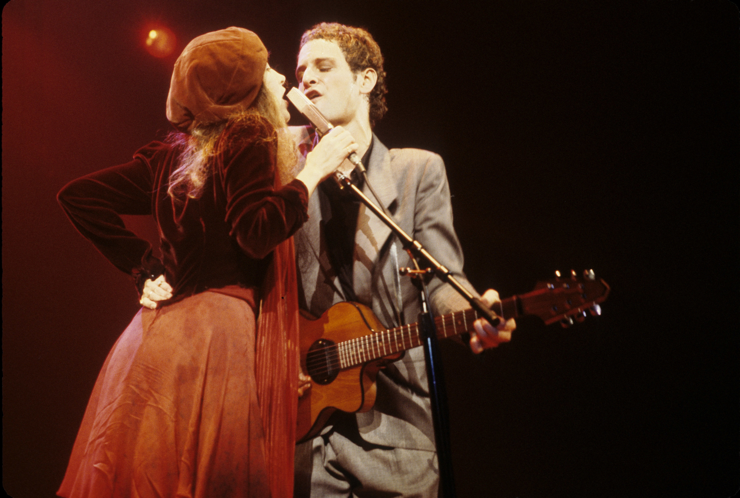 Stevie Nicks and Lindsey Buckingham on stage, singing passionately into the same mic with their faces close together