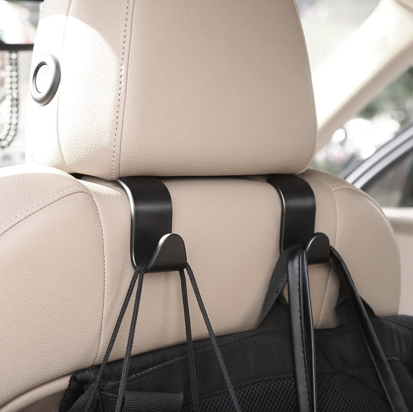 the black hooks holding several black bags on the back of a tan leather car seat