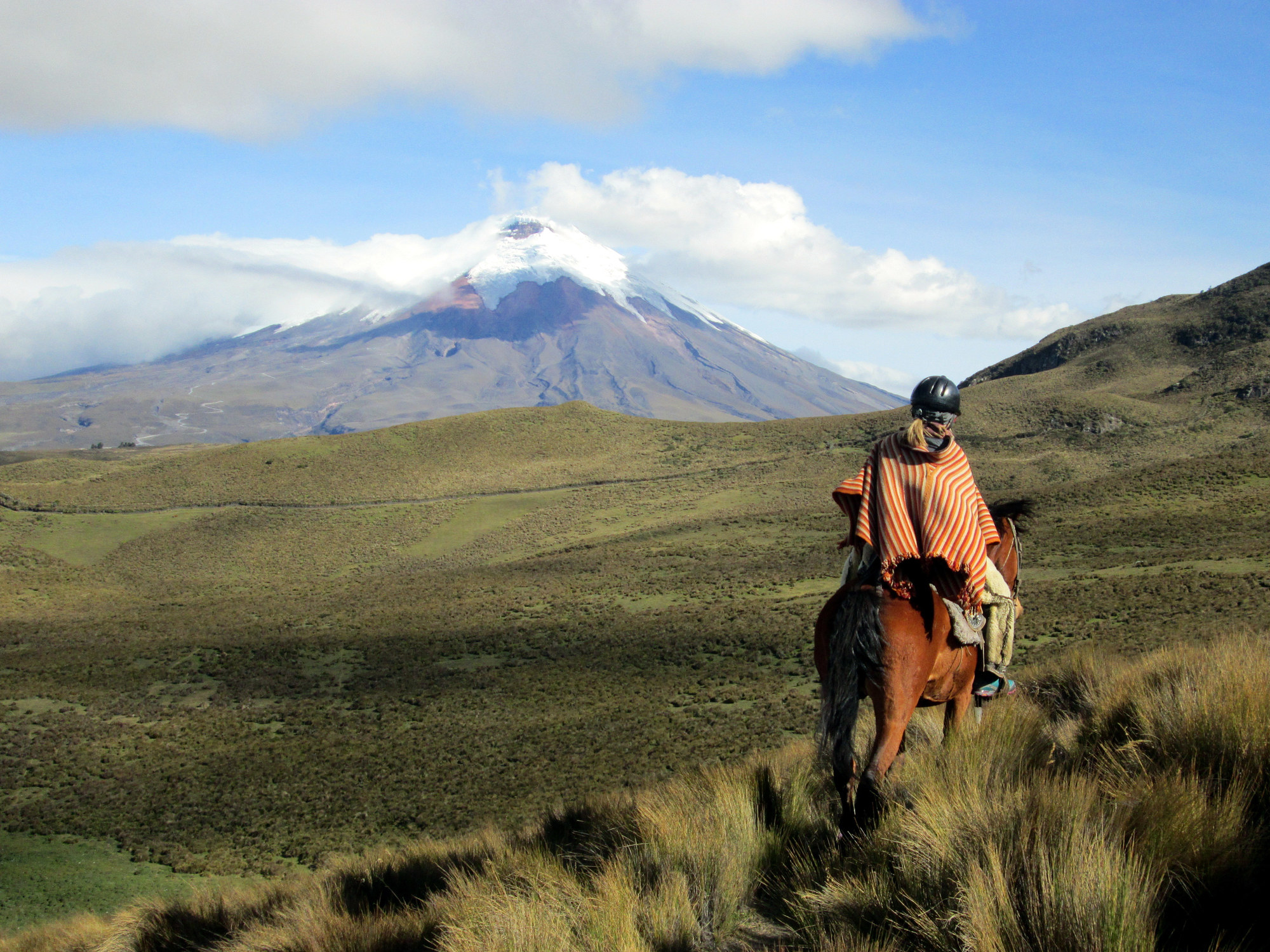 A person riding a horse in an Ecuadorian poncho.