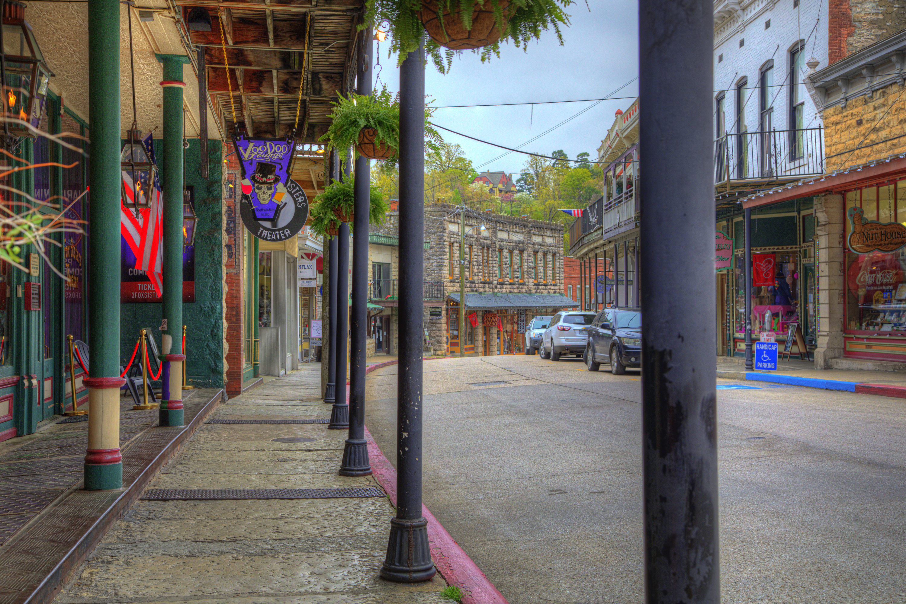 A street in Eureka Springs lined with various shops. One of the signs that says &quot;VooDoo&quot; above a storefront features a skull in a top hat