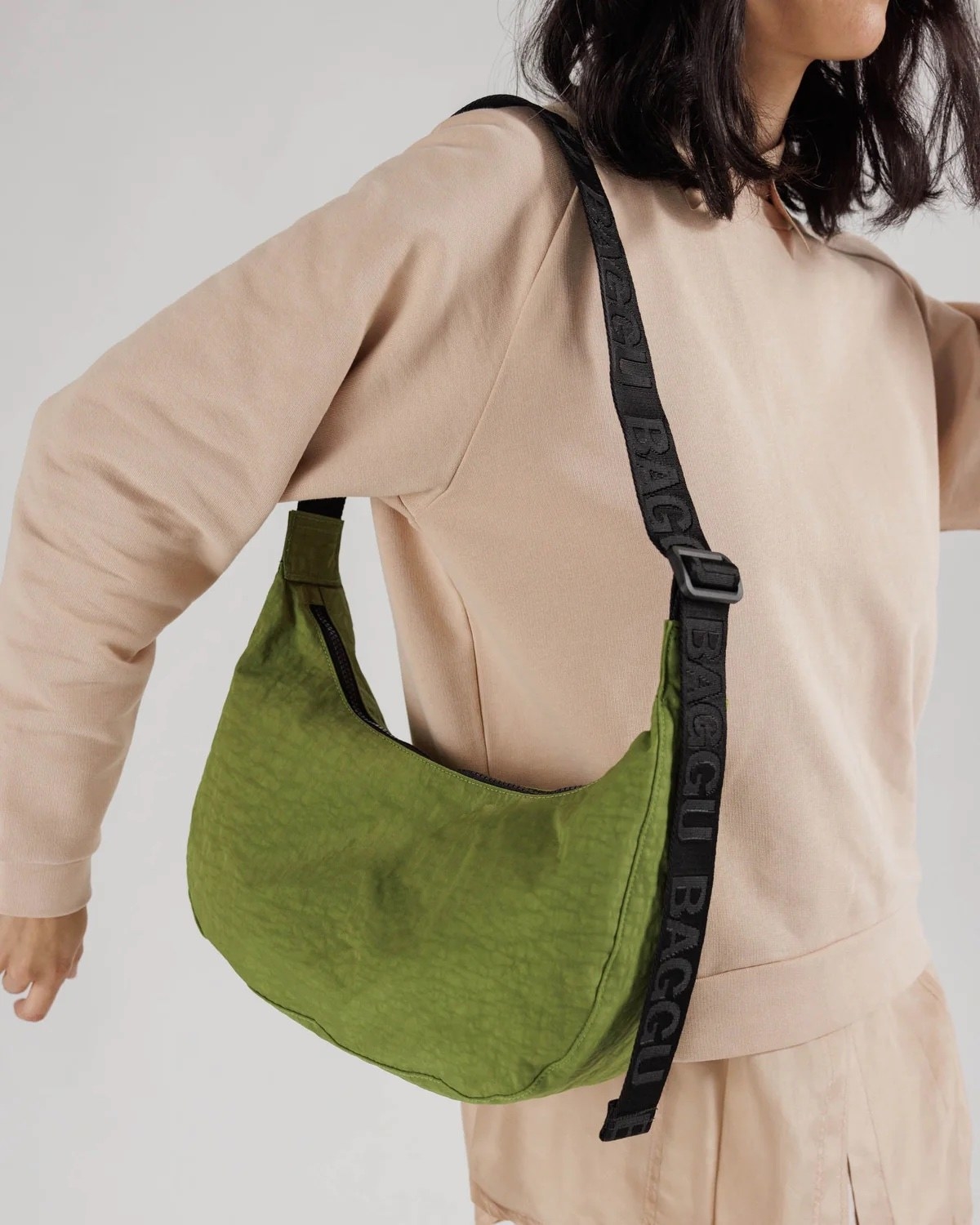 model wearing green crssbody crescent-shaped bag with an adjustable black nylon strap