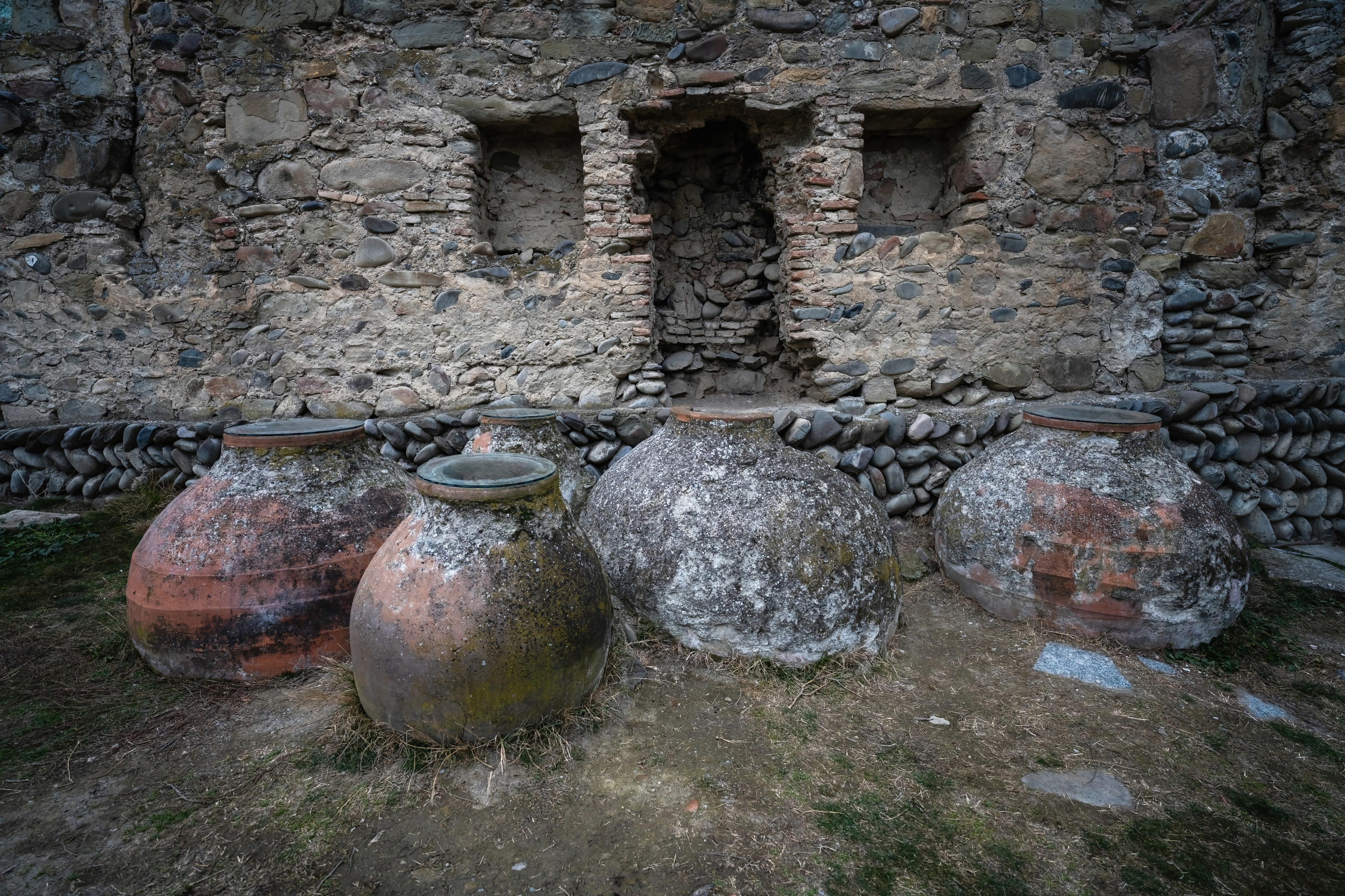 Old clay pots of wine nestled into the ground outside a stone building in Georgia