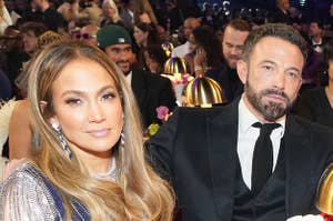 Jennifer Lopez sits with her hand wrapped around her knee and smiles as Ben Affleck appears bored sitting next to her