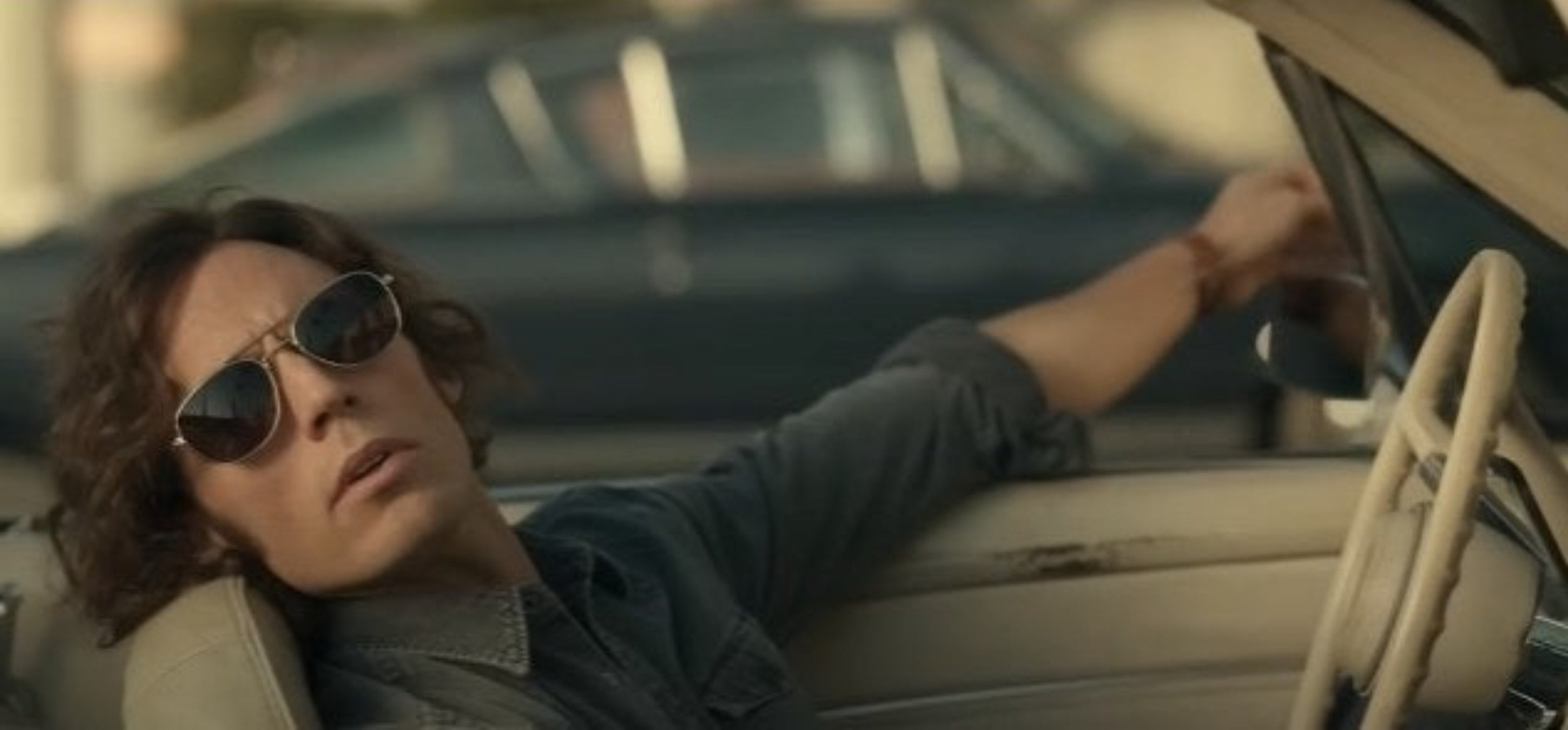 Sam Claflin as Billy Dunne, leaning back in the driver&#x27;s seat of a parked car, wearing sunglasses