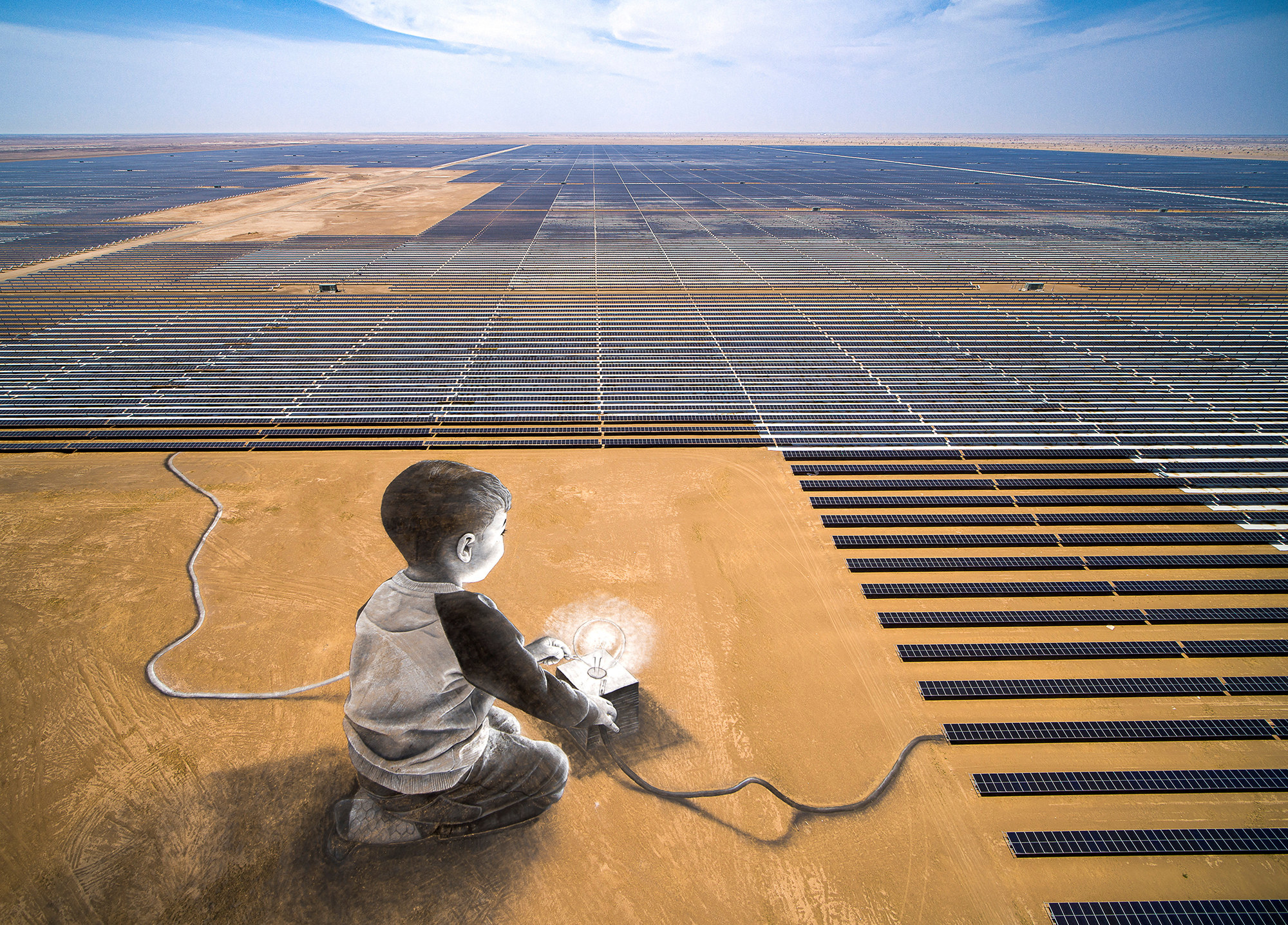 aerial view of a solar power farm in a desert area, in the bottom left there is a painting on the ground of a child and a light bulb