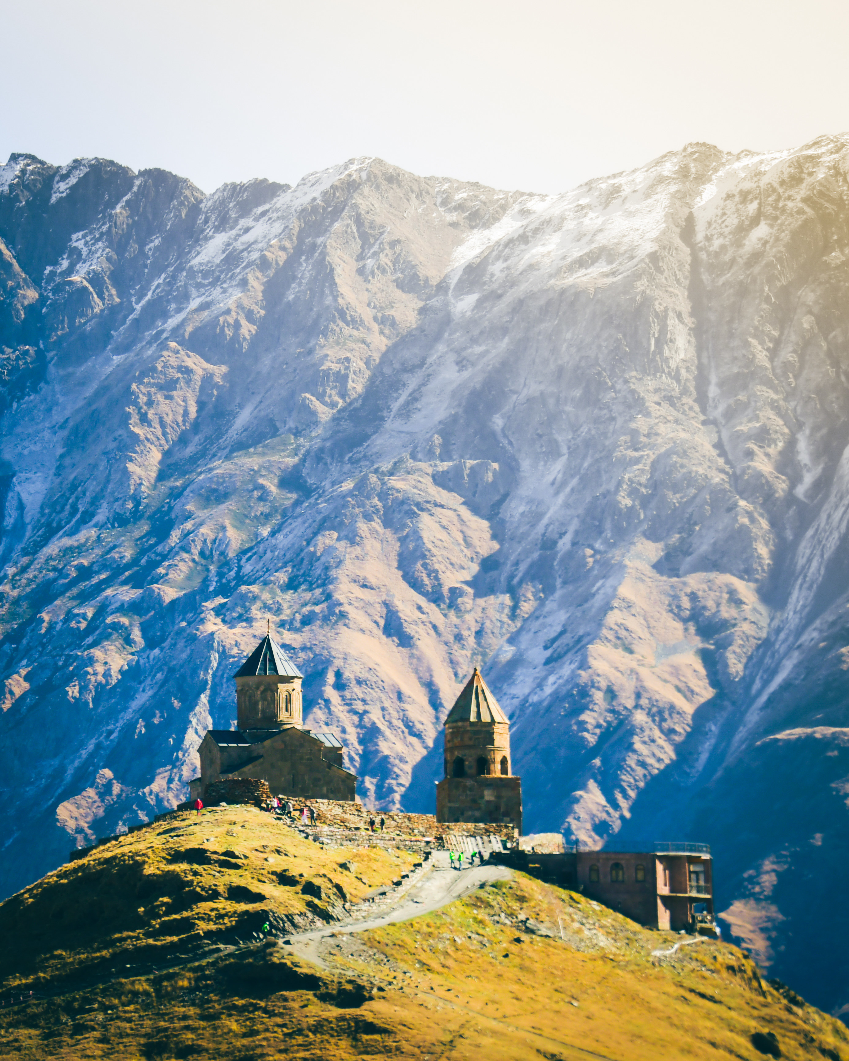 Short turreted buildings on a grassy hill in front of high snowy mountains