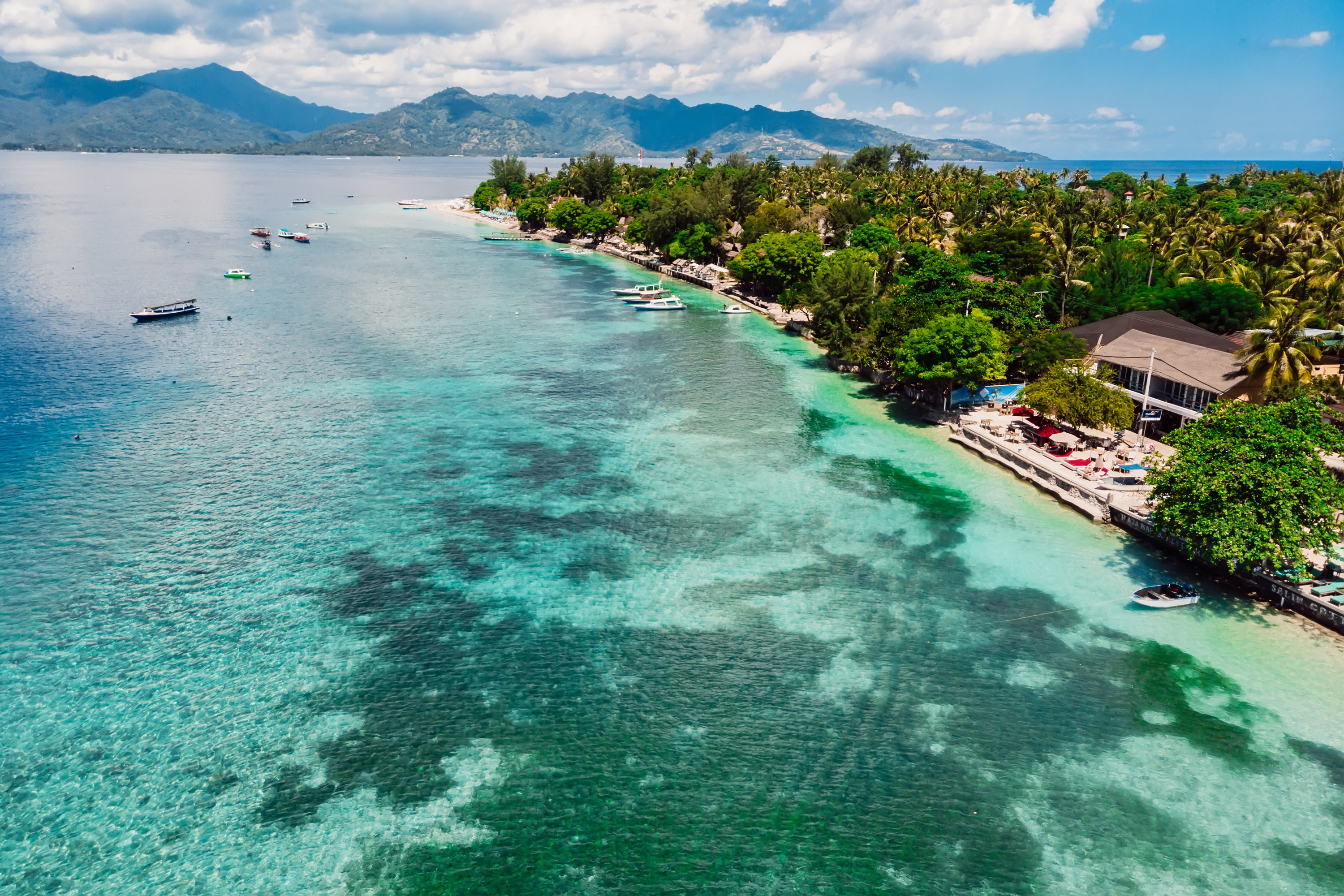 Shoreline of a tropical island with boats in the water and mountains in the background