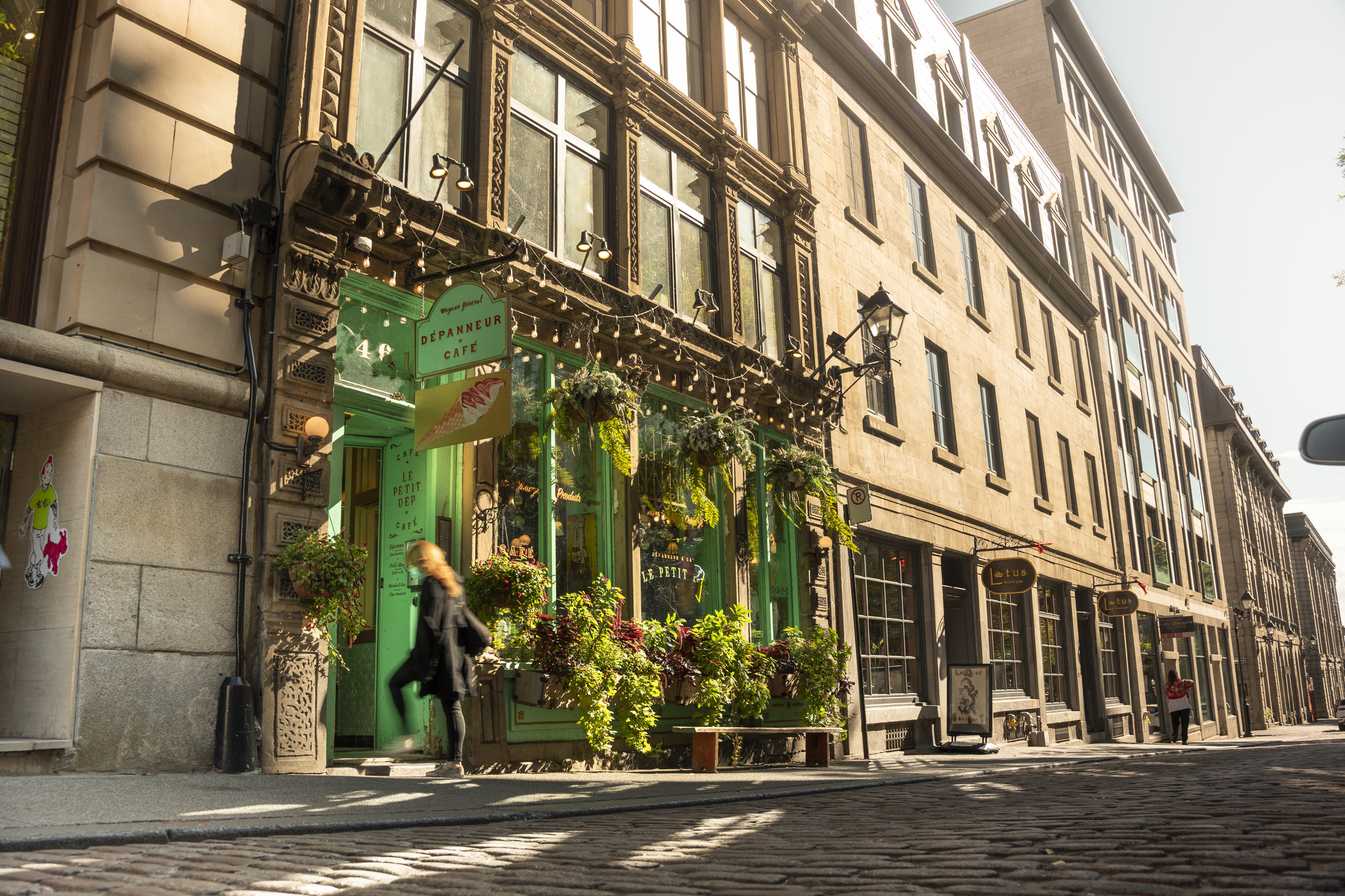 People walk on the cobblestone streets by a cafe and trendy restaurants and shops in the historic Old Town of Montreal