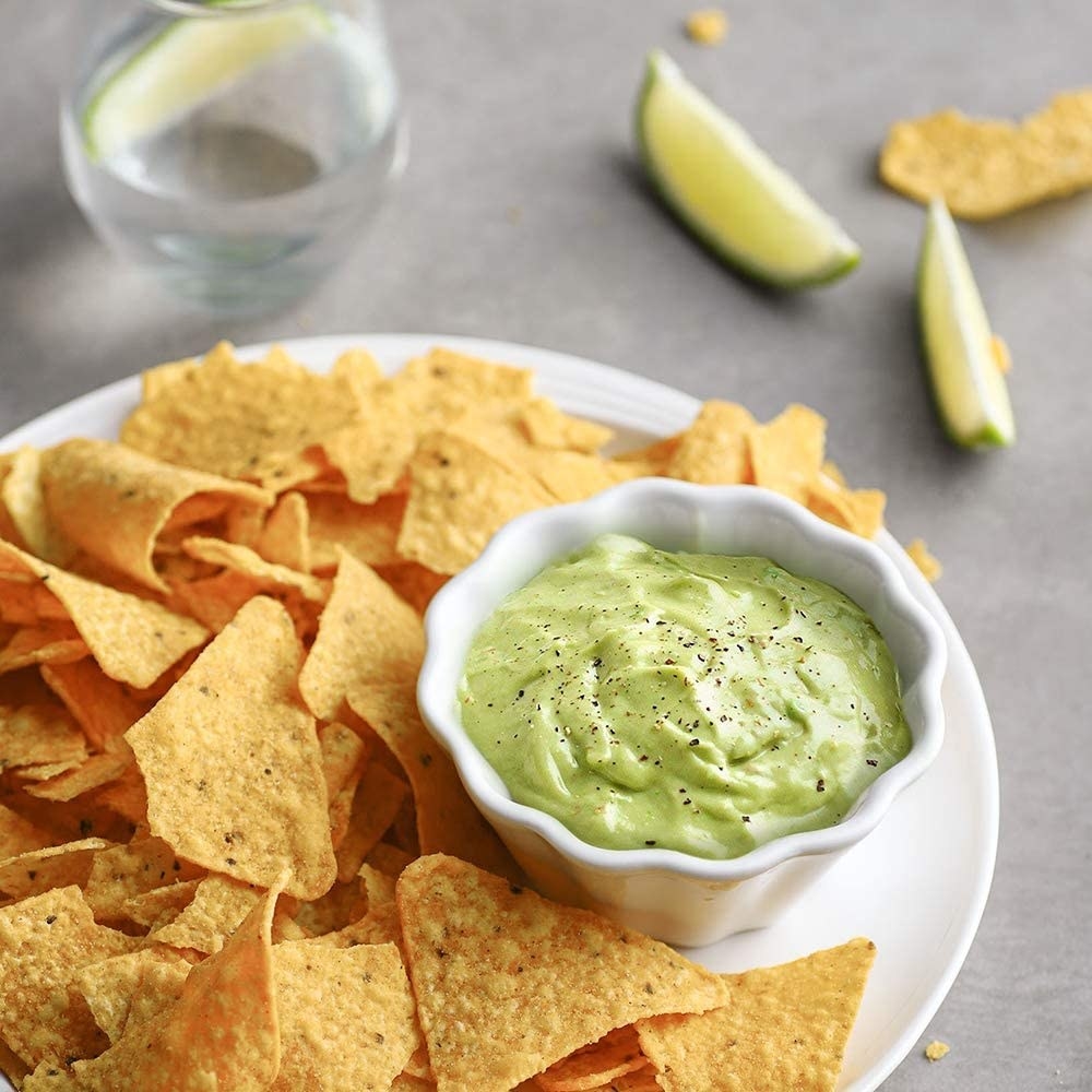 A flower-shaped ramekin on a plate with chips with guac inside
