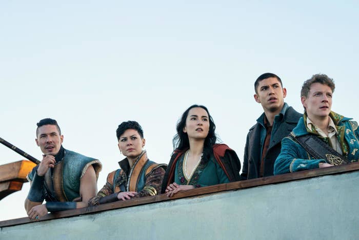 Five of the cast members stand at the side of a boat