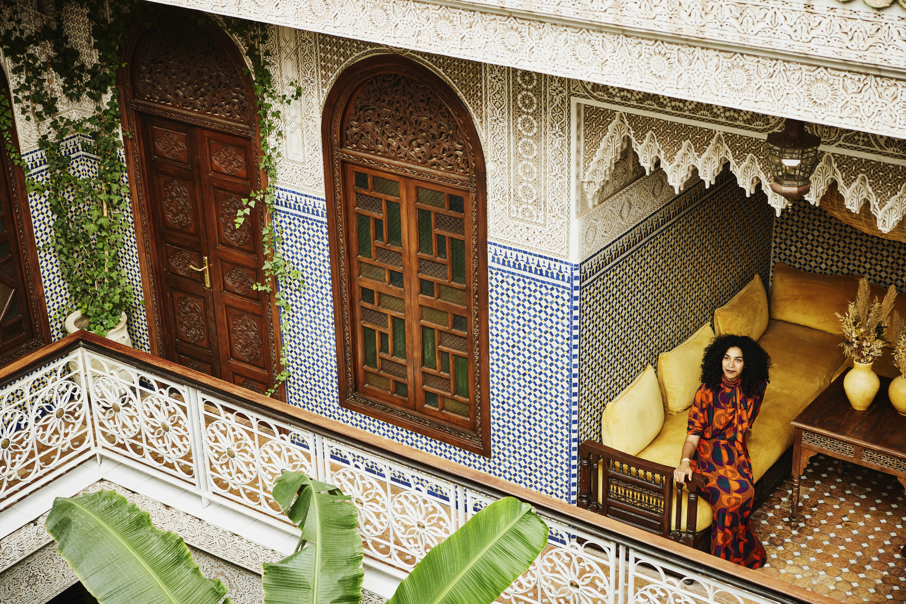 Wide shot elevated view of woman relaxing in alcove of ornately decorated riad