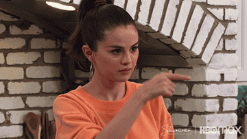 Selena Gomez on her cooking show making a gesture for &quot;call me&quot; in her kitchen