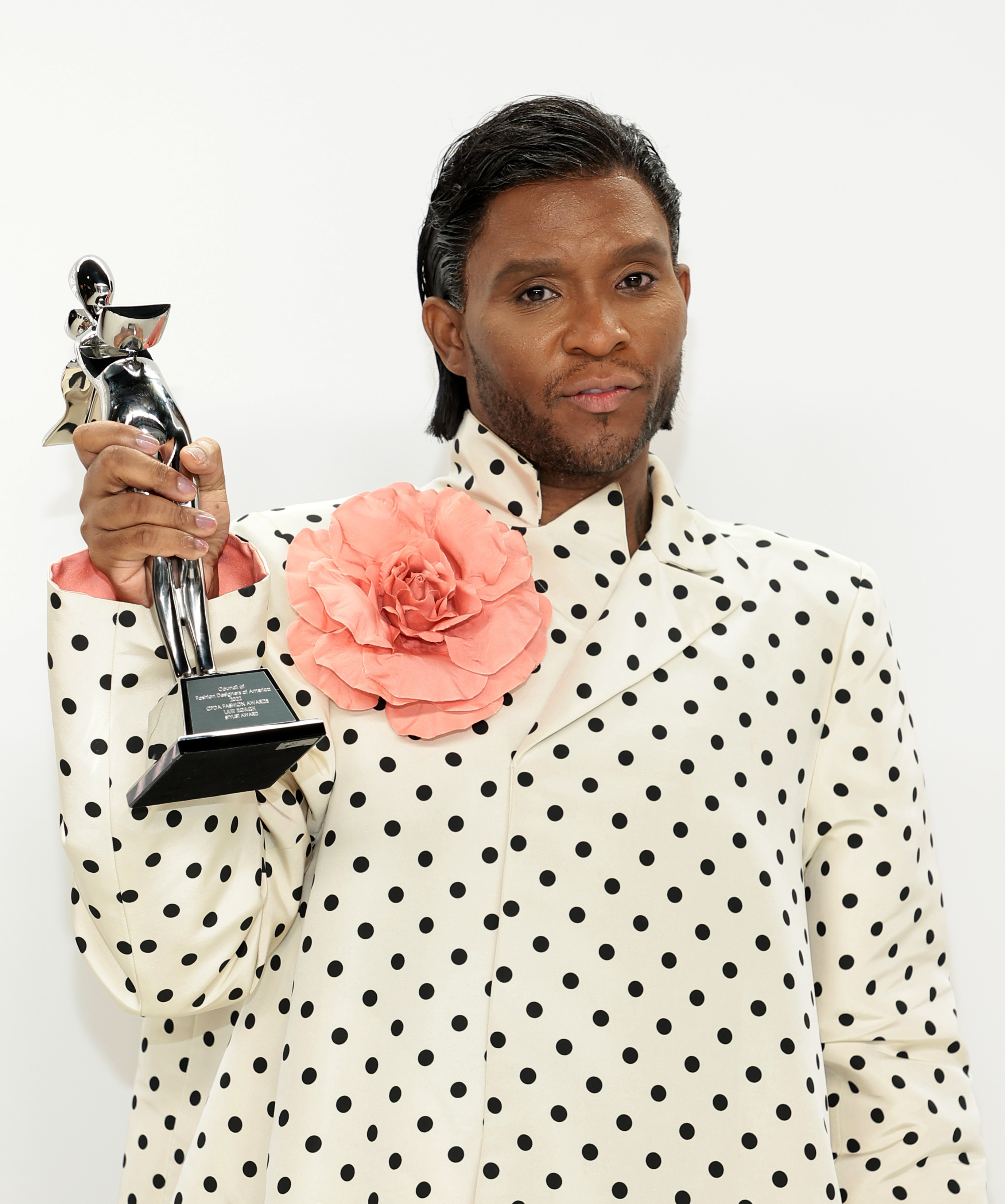 Law holding up an award while wearing a polka dot outfit with a large flower pinned to the front