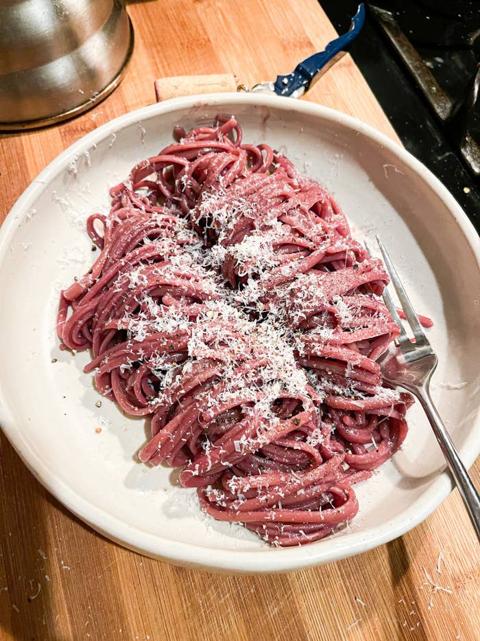 Red wine spaghetti on a white plate, sprinkled with parmesan cheese.
