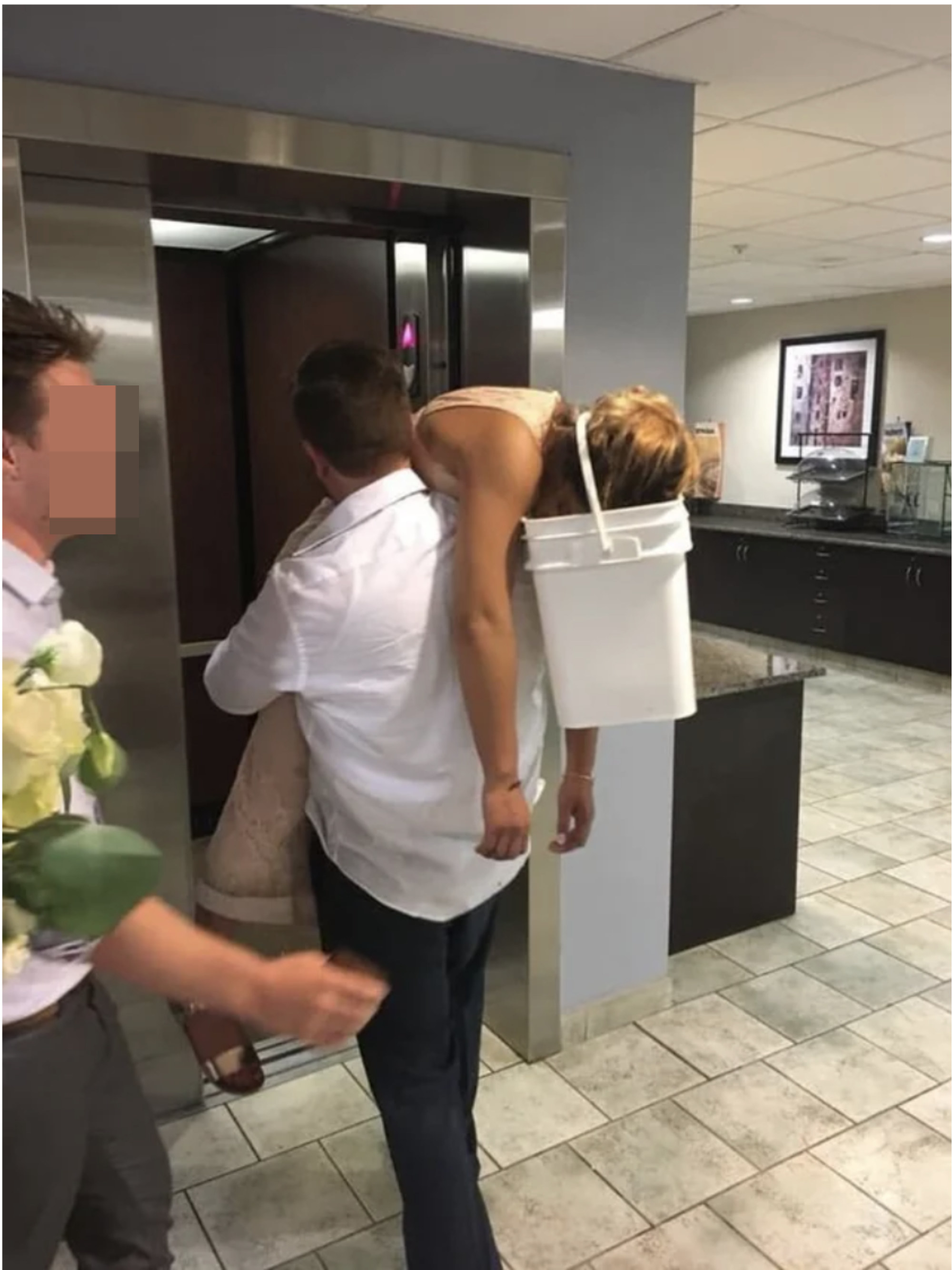 A man holding a passed out bride who has a bucket on her head