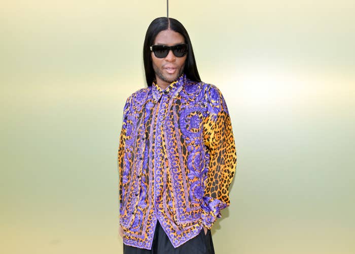 Torso shot of Law Roach, wearing a lilac and orange leopard print shirt and black sunglasses, his long hair parted in the centre and worn behind his shoulders