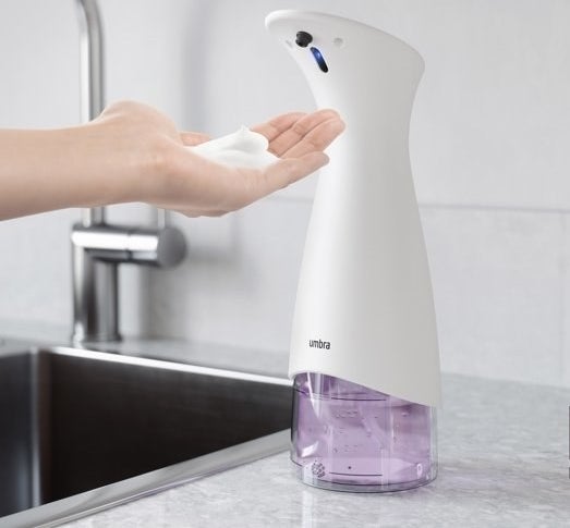 a person using a pink and white automatic soap dispenser on a granite kitchen counter