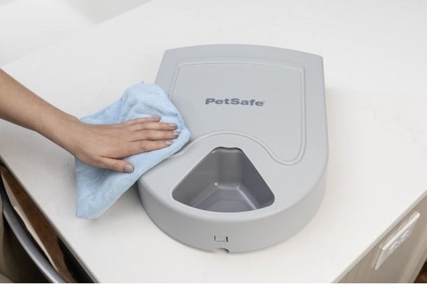 a person cleaning a gray automatic pet feeder on a kitchen counter