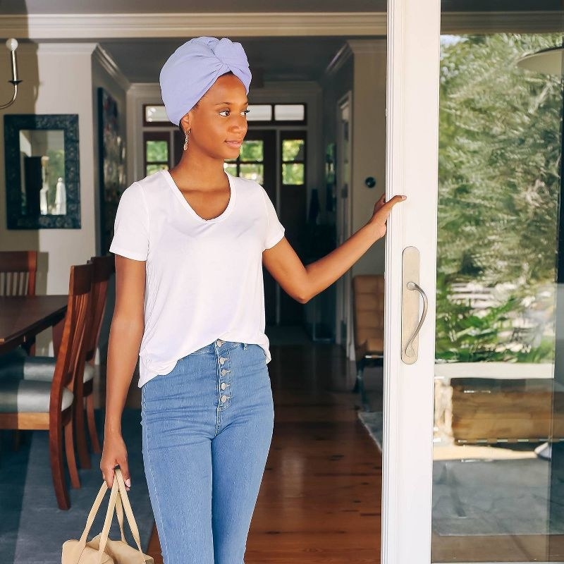 A person wearing a hair towel turban, jeans, a white tee, and carrying a brown bag
