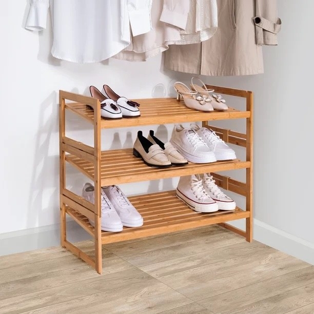 a bamboo three-tier shoe rack on a hard-wood floor against a white wall